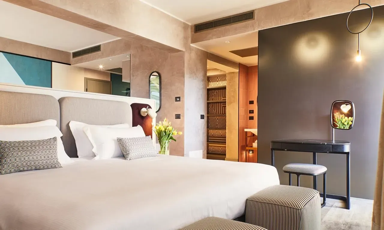 A bright suite with a large bed, soft grey headboard, warm wood and a small desk in contemporary art deco style.